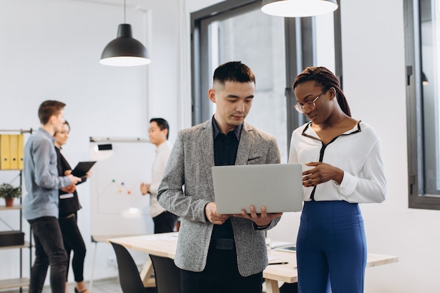 Foto afrikaanse onderneemster en aziatische zakenman die laptop met interracial groep zakenlieden & vrouwenteam met behulp van