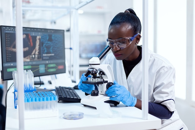 Afrikaanse onderzoeker die microscooplenzen aanpast die naar het monster op glasplaatje kijken. Zwarte gezondheidswetenschapper in biochemisch laboratorium met steriele apparatuur.