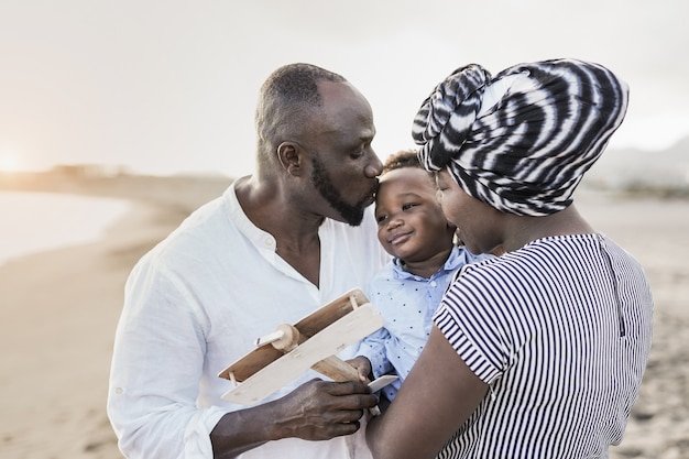 Afrikaanse ouders die zoontje buiten op het strand kussen - Familieliefde en vakantieconcept