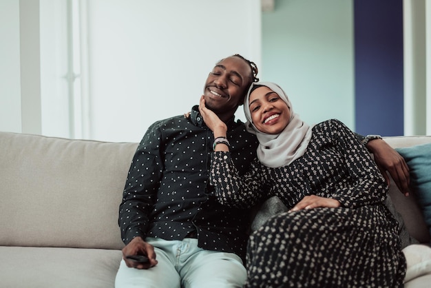 Afrikaanse Paar Zittend Op De Bank Samen Tv Kijken. Vrouwen die islamitische hijab-kleding dragen. Foto van hoge kwaliteit