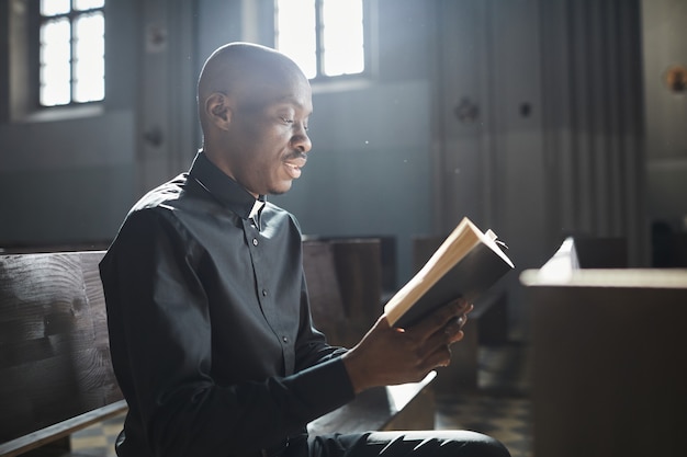 Afrikaanse priester in kraag die de Bijbel leest die voor altaar in de kerk staat