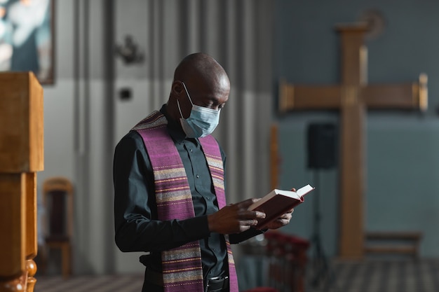 Afrikaanse priester met masker die de Bijbel leest en de ceremonie in de kerk houdt