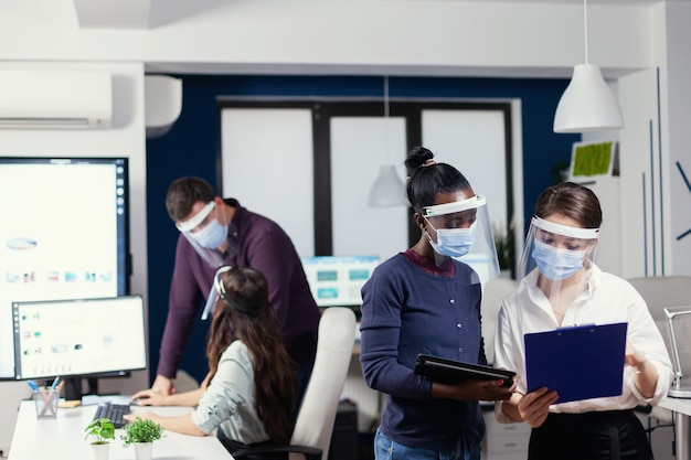 Afrikaanse projectmanager in gesprek met werknemer die gezichtsmasker draagt tegen covid19. Multi-etnisch zakelijk team dat werkt met respect voor sociale afstand tijdens wereldwijde pandemie met coronavirus.