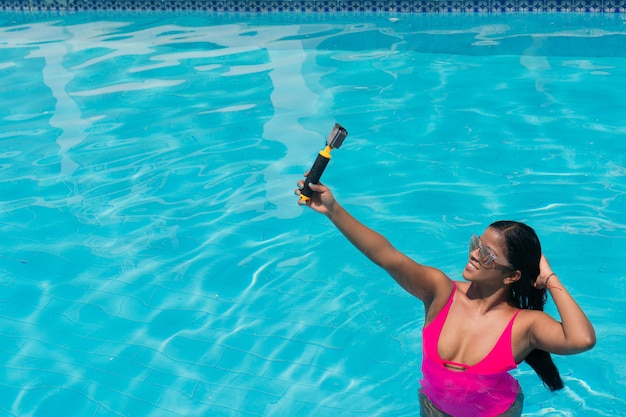 Afrikaanse reisblogger die selfie-foto maakt met actiecamera in een zwembad.