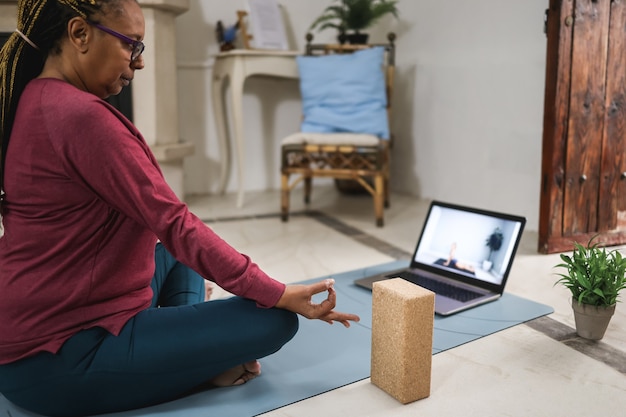 Afrikaanse senior vrouw doet online yoga les thuis - focus op hand
