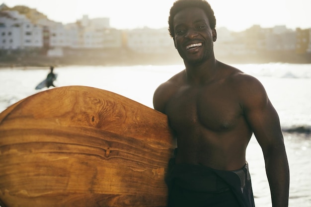 Afrikaanse surfer man met vintage surfplank op het strand bij zonsondergang Focus op gezicht