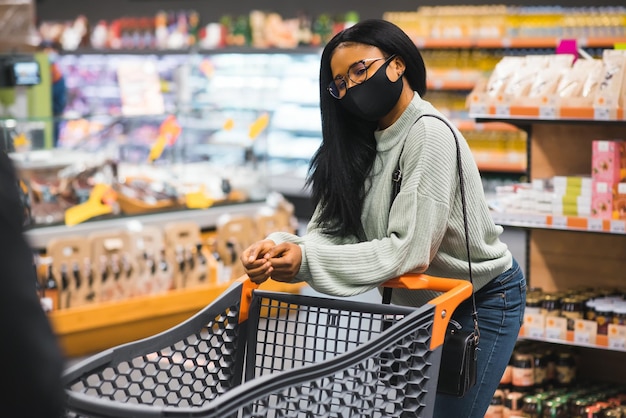 Afrikaanse vrouw die een medisch wegwerpmasker draagt dat in de supermarkt winkelt tijdens de uitbraak van de coronaviruspandemie Epidemische tijd