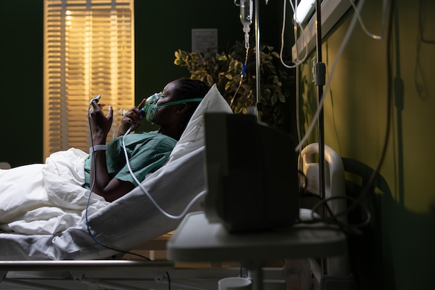 Foto afrikaanse vrouw in het ziekenhuis ligt in bed met een zuurstofmasker.