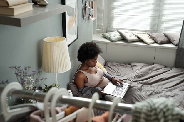 Afrikaanse vrouw in ondergoed netwerken met laptop in bed