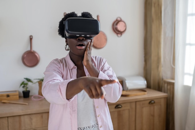 Afrikaanse vrouw in roze kleren in vr-bril ziet er opgewonden uit