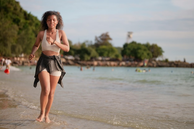 Afrikaanse vrouw in sportbeha loopt op het strand voor buitentraining Portret sexy Aziatische Afrikaanse dame bereidt zich voor op fitness op het strand