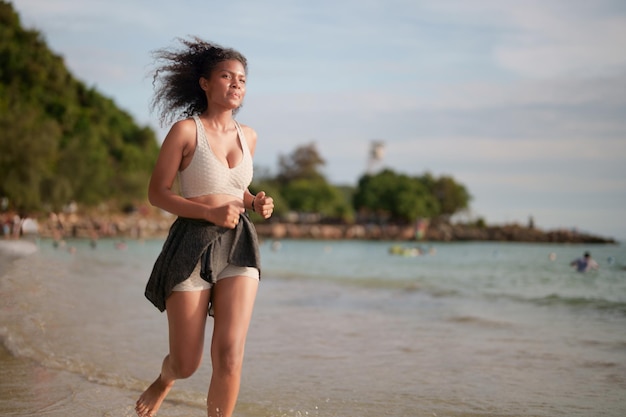 Afrikaanse vrouw in sportbeha loopt op het strand voor buitentraining Portret sexy Aziatische Afrikaanse dame bereidt zich voor op fitness op het strand