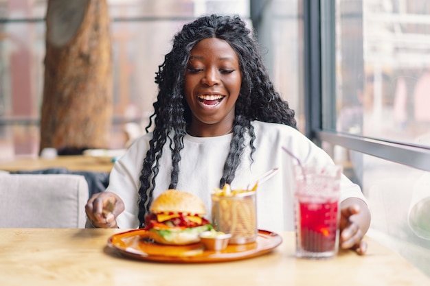 Afrikaanse vrouw met afrohaar die een smakelijke klassieke hamburger met frietjes eten. dieet ondermijnende maaltijd.