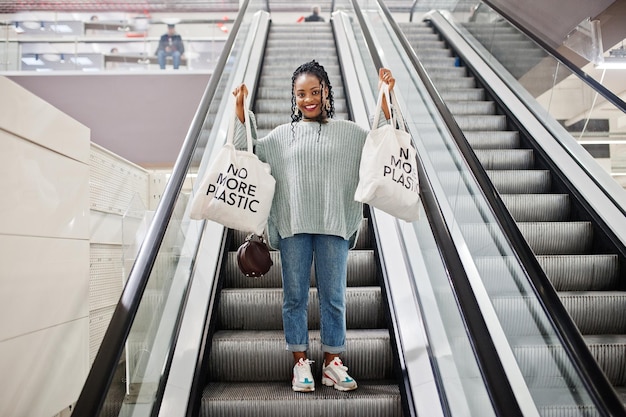 Afrikaanse vrouw met eco-winkeltassen op roltrap in winkelcentrum