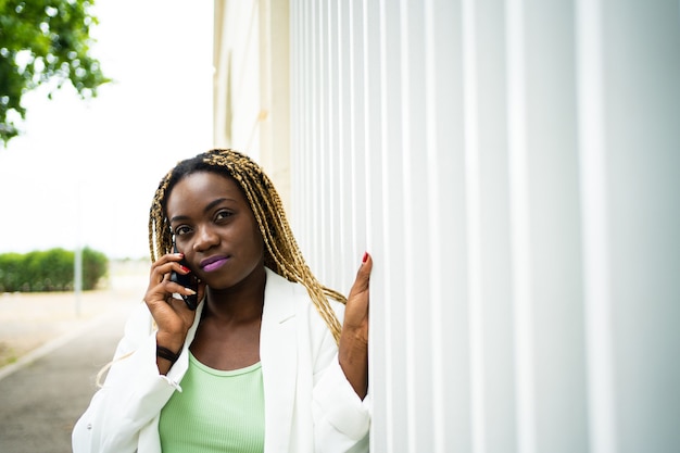 Afrikaanse vrouw met vlechten en formele kleding in gesprek met mobiel buitenshuis