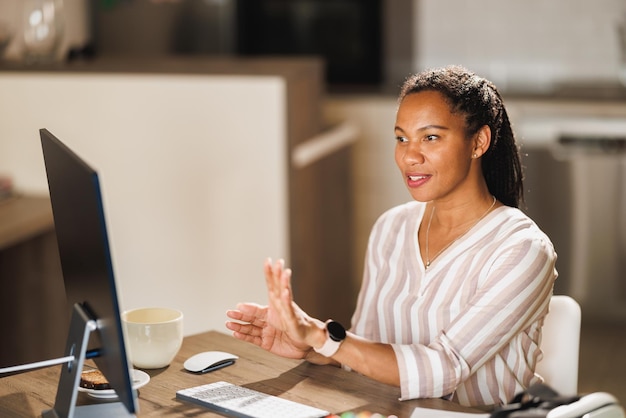 Afrikaanse vrouwelijke freelancer die een computer gebruikt en online vergadert terwijl ze vanuit haar thuiskantoor werkt.