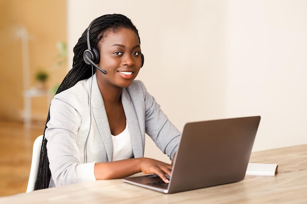 Afrikaanse vrouwelijke klantenserviceoperator die een headset draagt en op een laptop werkt