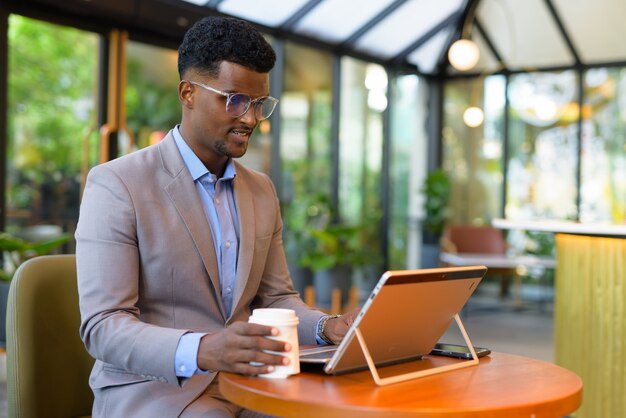 Afrikaanse zakenman in café-restaurant met behulp van laptopcomputer en koffiekopje te houden