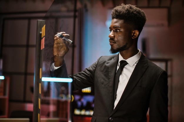 Afrikaanse zakenman in formele kleding die een todo-lijst schrijft van het nieuwe project op de glazen wand van het kantoor