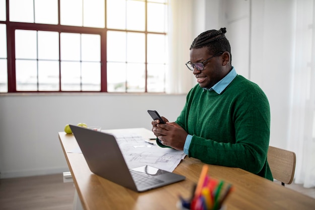 Afrikaanse zakenman met behulp van app via mobiele telefoon zittend op de werkplek