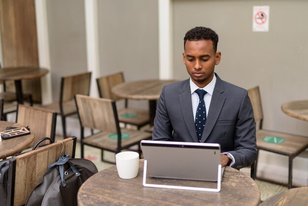 Afrikaanse zakenman met behulp van laptop terwijl sociale afstand nemen bij coffeeshop