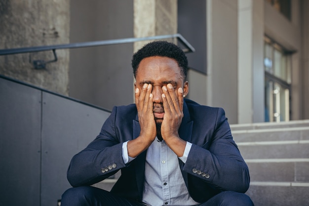 Afrikaanse zakenman zit gefrustreerd op de trap, depressief door de resultaten van zijn werk, hand in hand achter zijn hoofd