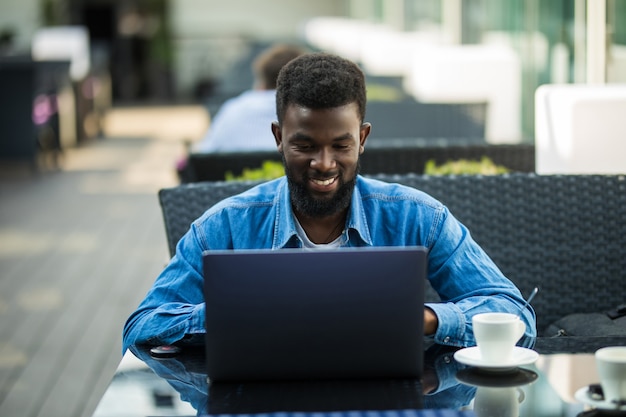 Afrikaanse zakenman zittend aan tafel in café werken met laptop en papieren en koffie drinken