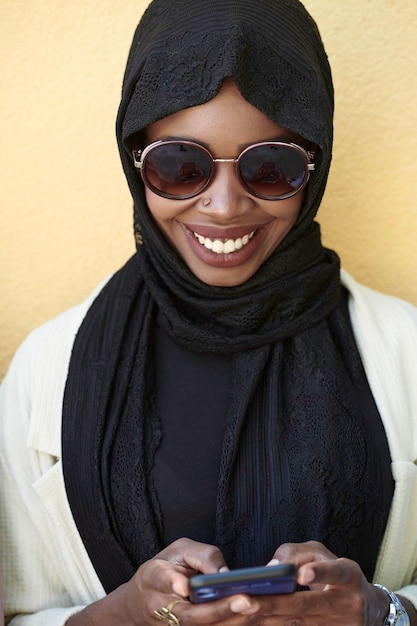 Afrikaanse zakenvrouw die een smartphone gebruikt die traditionele islamitische kleding draagt