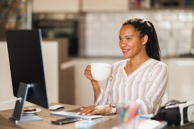 Afrikaanse zakenvrouw genieten van een kopje koffie terwijl ze thuis werkt.
