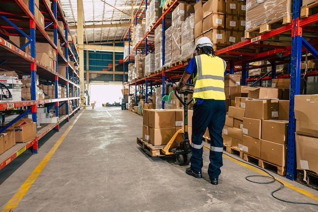 Afrikaanse zwarte magazijnwerker die pakketpallet gebruikt om lading te verplaatsen voor logistiek, scheepvaart en supply management.