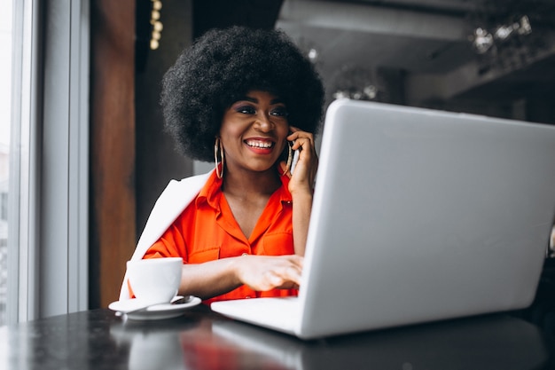Afro american business woman in white suit working on laptop in a cafe