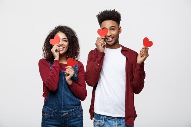 Afro American couple holding two red paper heart, looking at camera and smiling