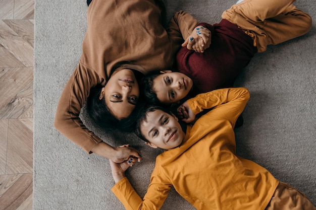 Afro American Family Mom and Two Sons Lie on the Floor and Look at the Camera Top view