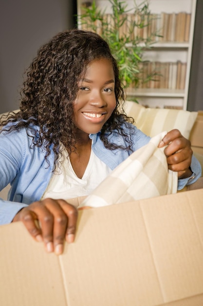Афроамериканка собирает вещи в коробку для переезда в новый дом темнокожая девушка собирается ...