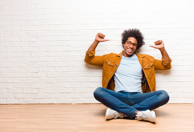 an afro-american guy sitting looking satisfied and successful while pointing to self