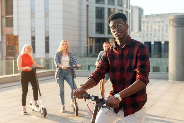 Afro american guy with an electric scooter in the company of friends in the city