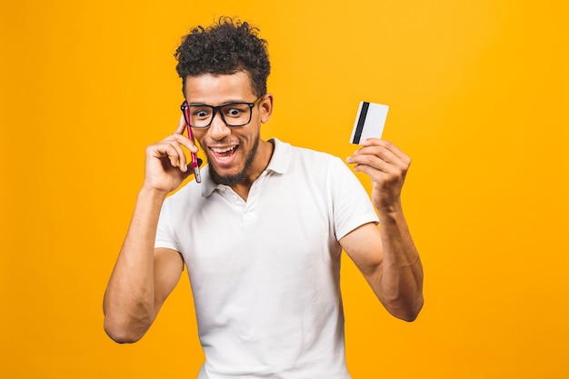 Afro american man dressed in casual, using mobile phone, showing plastic credit card 