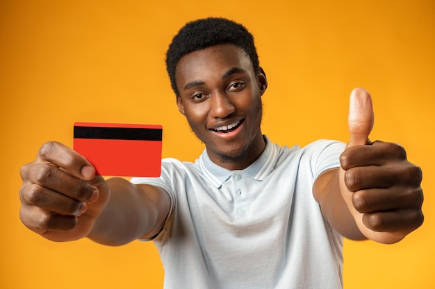 Photo afro american man holding red credit card against yellow background in studio