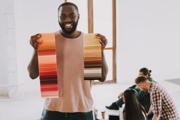 L'uomo afroamericano sta tenendo le tavolozze dei colori e sta sorridendo.