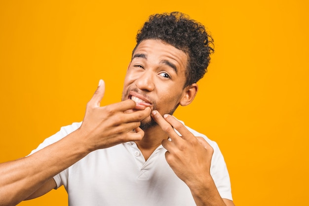 Afro american man is squeezing pimples on his forehead while\
looking into the mirror in bathroom