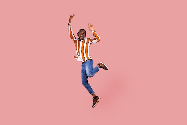 アフリカ系アメリカ人の男がポーズをとってジャンプし、勝利のジェスチャーを示し、彼の勝利を祝います。