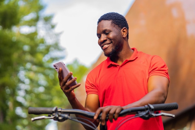 Afro american man in red tshirt walking in park with a bicycle