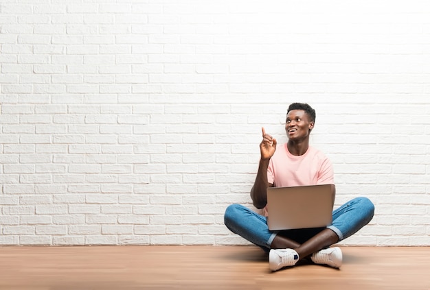 Uomo afroamericano che si siede sul pavimento con il suo computer portatile che indica con il dito indice una grande idea