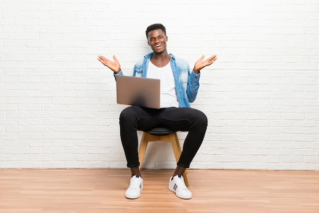 Афро-американский мужчина работает с ноутбуком с удивлением и шокирован выражением лица