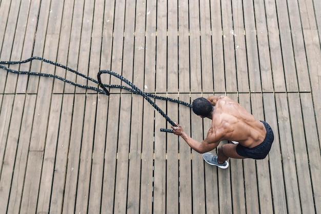 Afro American muscular man exercising with heavy ropes Photo of handsome man with perfect body Strength and motivation aerial view