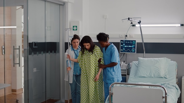 Afro american nurse with doctor helping patient to stand up from bed