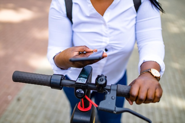 アフリカ系アメリカ人の女性が路上でレンタルスクーターまたは自転車をアクティブにして前払いします