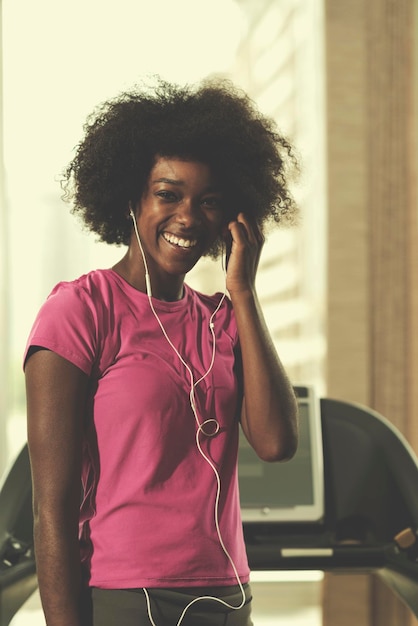 afro american woman running on a treadmill at the gym while listening music on earphones