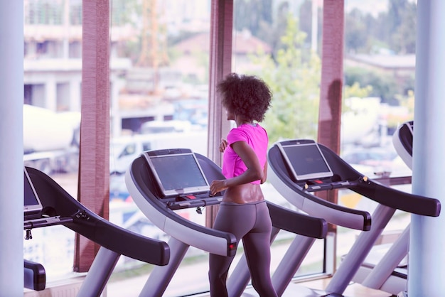 afro american woman running on a treadmill at the gym while listening music on earphones