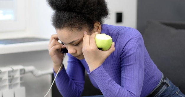 Afro American woman talking on a smartphone and eating an apple